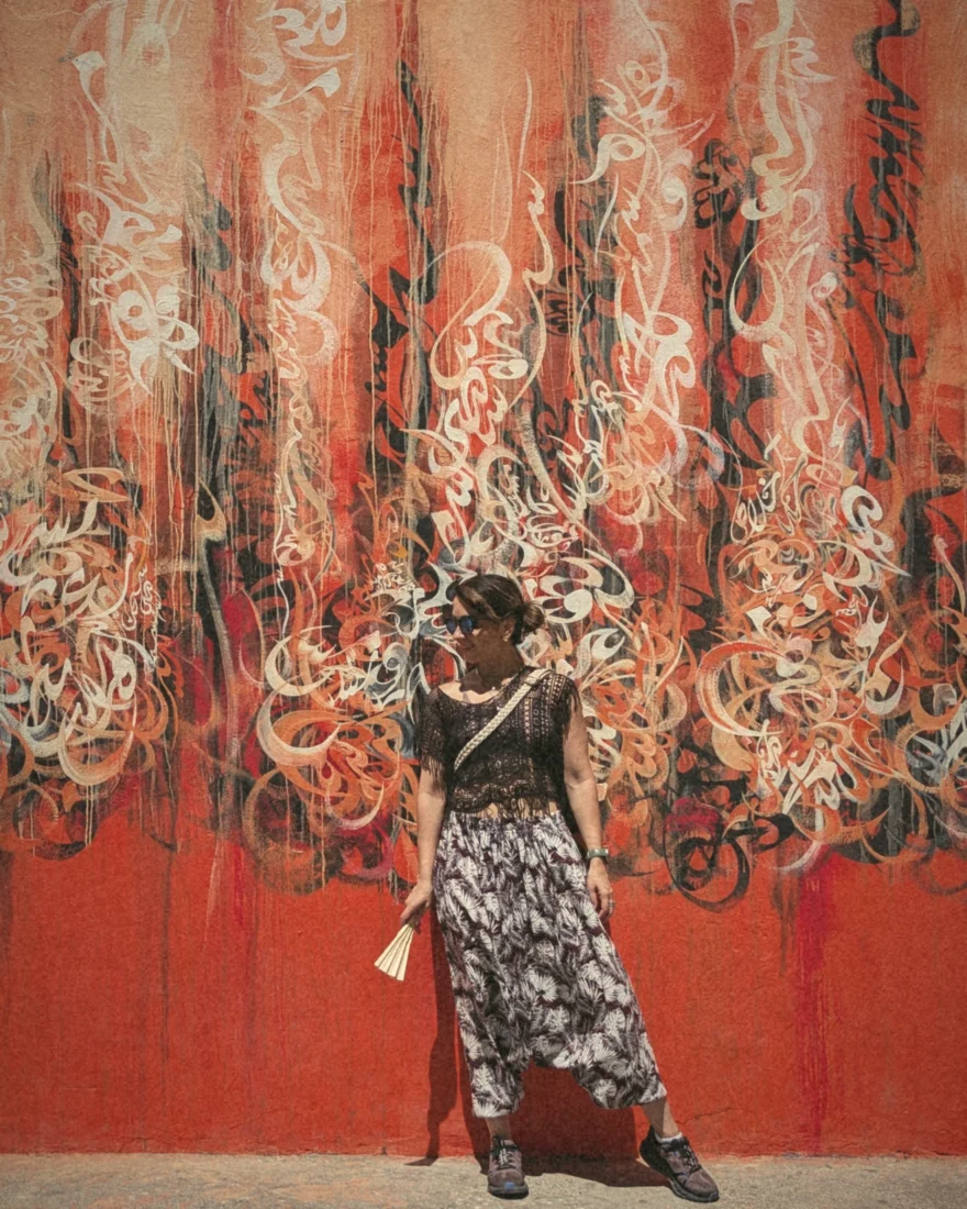 Saba in front of a large orange and red mural of flowing calligraphy
